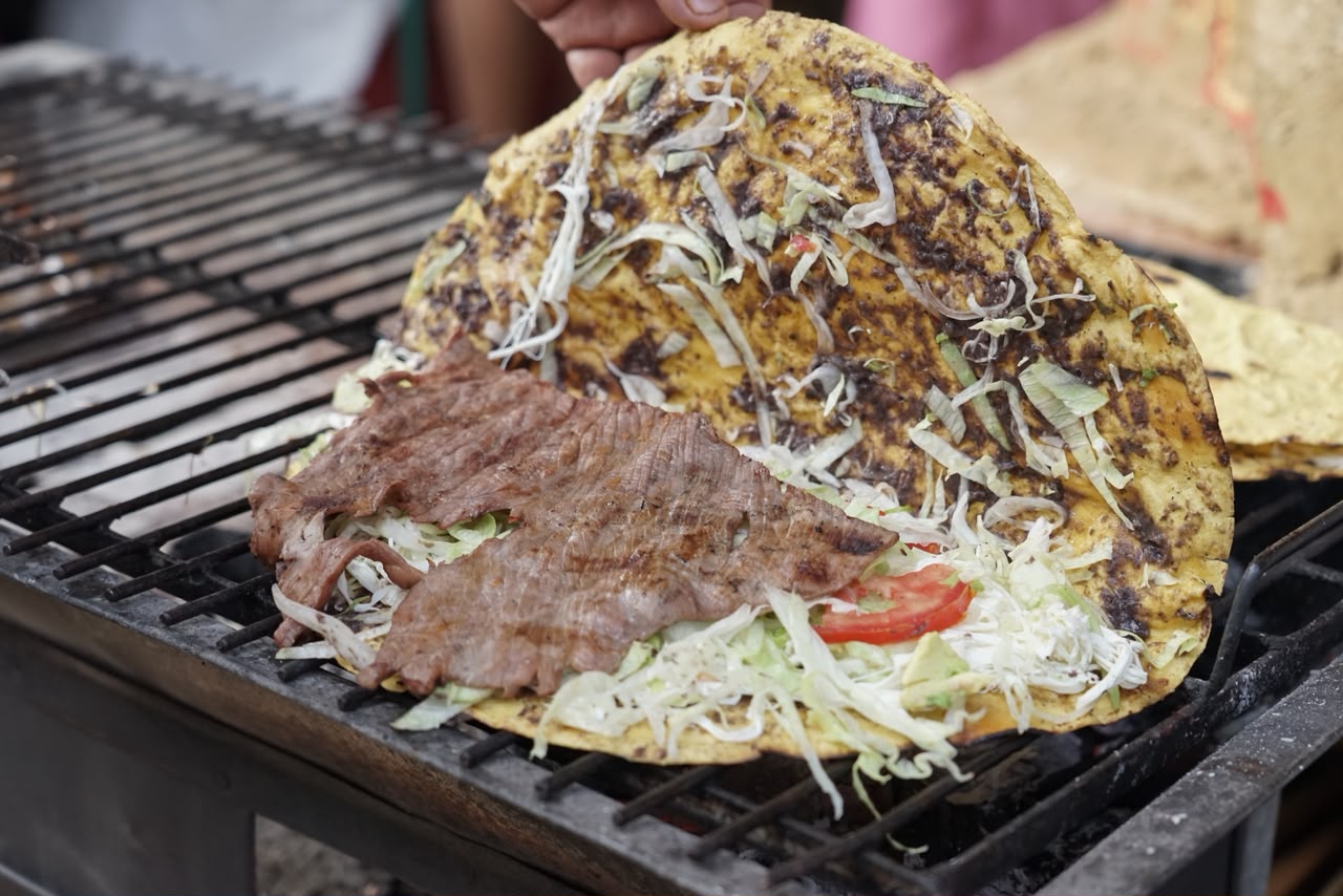 Tlayuda Oaxaqueña Tradicional Con Tasajo, Col Y Quesillo Calentándose Sobre Una Parrilla Al Carbón Durante La Feria De La Tlayuda.