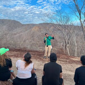 Sectur pide contratar guías de turistas certificados en méxico la revista del sureste mx Guía De Turistas Acreditado Explica Un Recorrido Al Aire Libre Frente A Un Grupo De Visitantes En Un Mirador Montañoso Durante Una Actividad De Senderismo En México, Rodeado De Paisaje Natural Y Cielo Parcialmente Nublado.