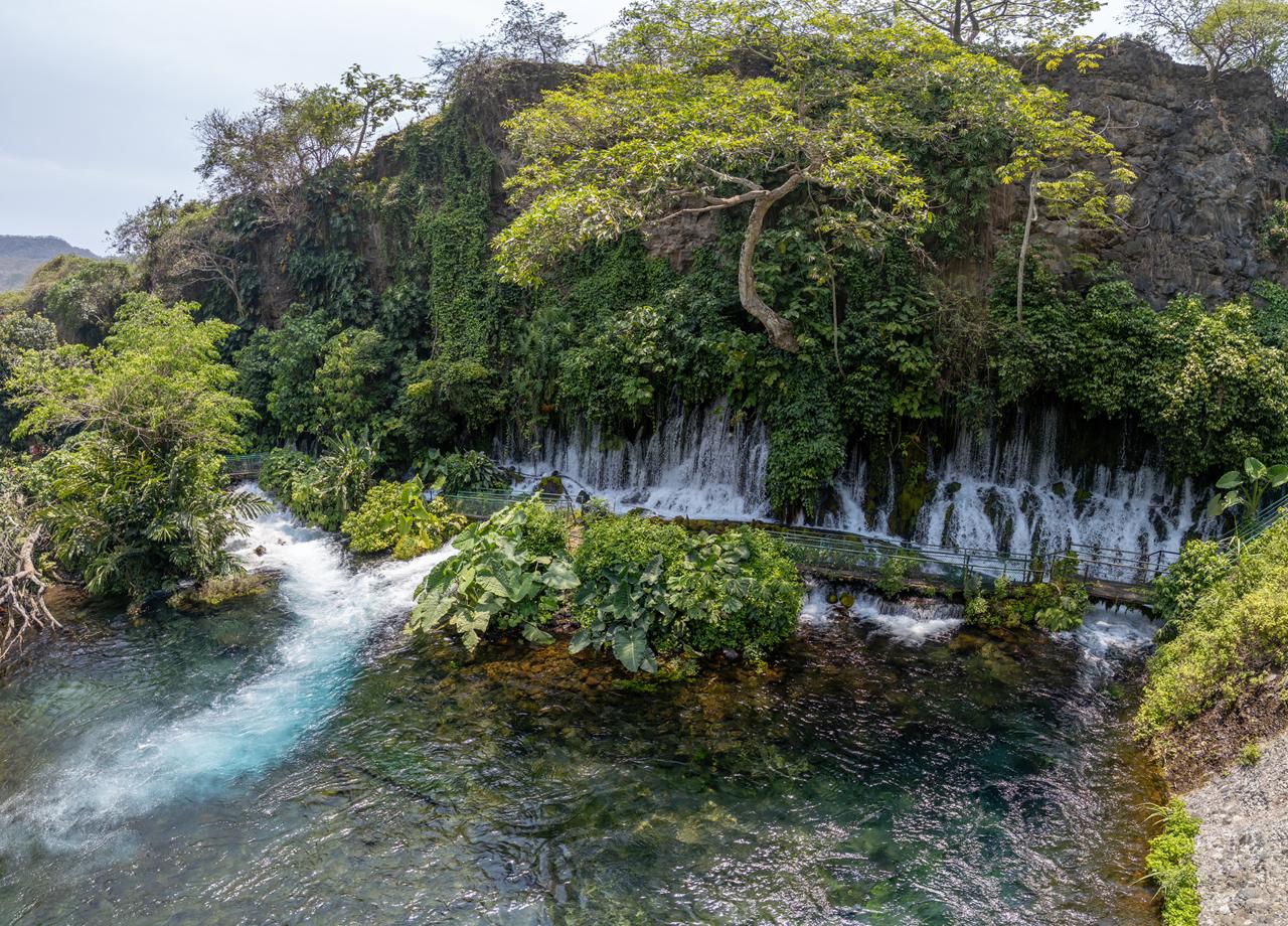 Región cultura y aventura: el corazón histórico de veracruz la revista del sureste mx Cascada Que Cae Sobre Un Cuerpo De Agua Cristalina Rodeado De Vegetación Selvática Y Paredes Rocosas, Con Una Pasarela De Madera.