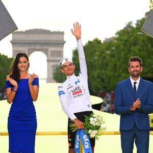 El Ciclista Mexicano Isaac Del Toro Saluda Desde El Podio Vistiendo El Maillot Blanco Como Campeón Joven Del Tour De Francia 2026, Con El Arco De Triunfo De París Al Fondo.