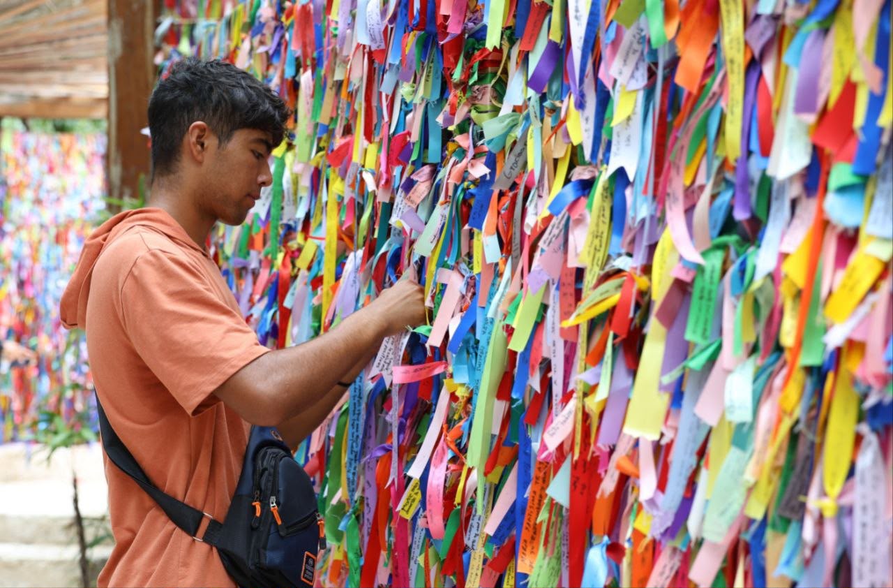 Un Joven Atando Un Listón De Color En El Muro De Peticiones Del Santuario De María Desatadora De Nudos, Lugar Clave Para El Turismo Religioso En Cancún.