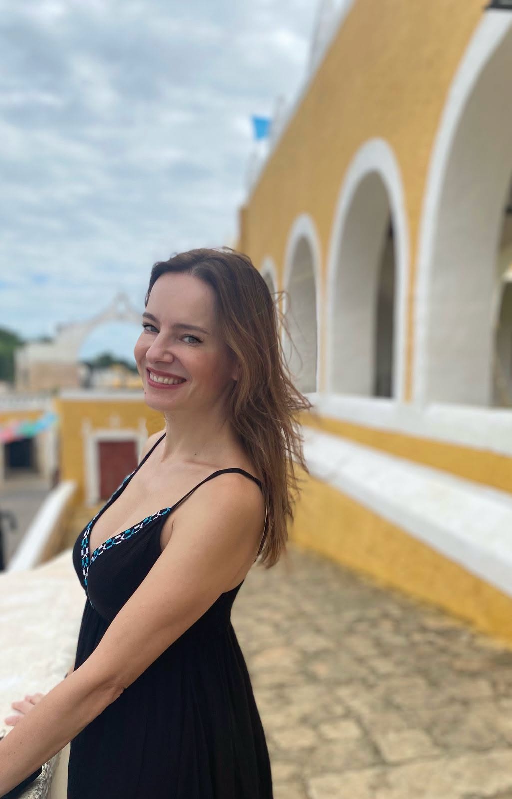 La actriz gaby platas queda enamorada de la magia colonial y costera de yucatán en una escapada inolvidable la revista del sureste mx La Actriz Gaby Platas Sonríe A La Cámara Vistiendo Un Vestido Negro De Tirantes Mientras Posa Junto A Los Arcos Amarillos Y Blancos Del Ex Convento De San Antonio De Padua En Izamal, Yucatán.