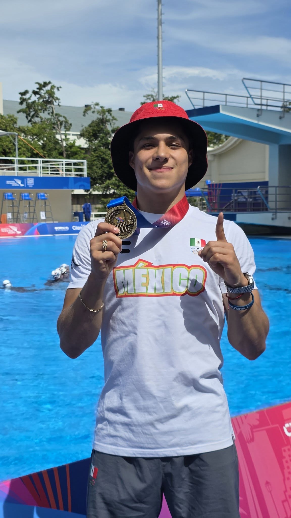 Adiós “¿y si sí? ”, hola “aquí sí”: osmar olvera sacude las redes tras ganar tres oros en santo domingo 2026 la revista del sureste mx El Clavadista Mexicano Osmar Olvera Posa Sonriente Junto A La Fosa De Clavados Vistiendo La Playera Oficial De México Y Mostrando Su Medalla De Oro Ganada En Los Juegos Centroamericanos Y Del Caribe 2026.