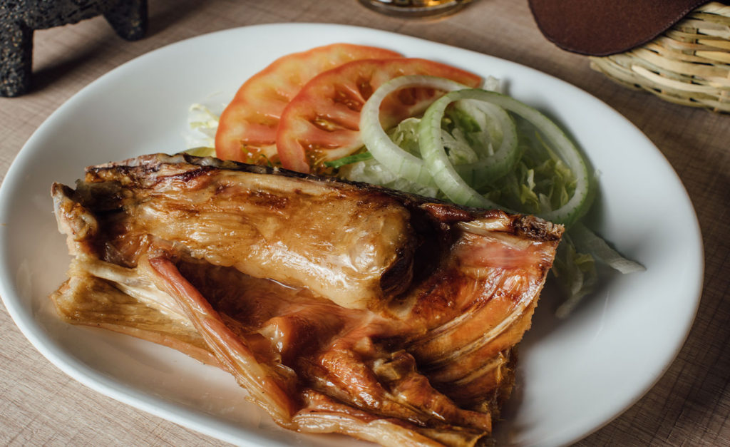 Sabor y tradición norteña: las 5 joyas gastronómicas que debes probar en tu visita a monterrey la revista del sureste mx Porción De Cabrito Al Pastor Bien Asado Y Dorado Servido En Un Plato Blanco, Acompañado De Ensalada Con Rodajas De Jitomate, Cebolla Y Lechuga.