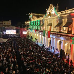 Fotografía Panorámica Nocturna De Una Plaza Pública Abarrotada Frente A Un Edificio Gubernamental Iluminado Con Motivos Patrios Durante Las Fiestas Del Grito De Independencia.
