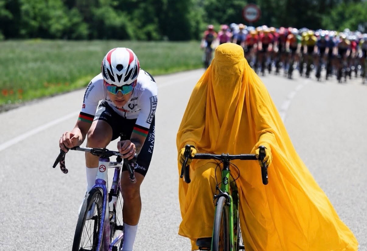 La Ciclista Afgana Fariba Hashimi Compitiendo En Bicicleta Junto A Otra Persona En Una Carretera, Simbolizando La Lucha Y La Realidad De Las Mujeres En Su País.