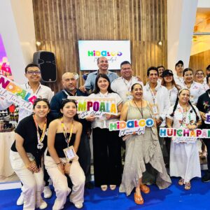 Un Grupo Grande De Aproximadamente 15 Personas Posa Sonriente Para Una Foto En El Interior De Un Stand De Exposición. Detrás De Ellos Hay Una Pared De Madera Y Una Pantalla Que Dice &Amp;Quot;Hidalgo ¡Tiene Algo!&Amp;Quot;. Varias Personas En El Grupo Sostienen Letreros Con Nombres De Lugares Como &Amp;Quot;Nopala&Amp;Quot;, &Amp;Quot;Cempoala&Amp;Quot; Y &Amp;Quot;Huichapan&Amp;Quot;, Y El Lema &Amp;Quot;Hidalgo ¡Tiene Algo!&Amp;Quot;. El Grupo Está Formado Por Hombres Y Mujeres De Diversas Edades, Vestidos Con Ropa Casual Y De Negocios, Algunos Con Gafetes.