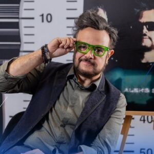 Retrato Del Cantante Aleks Syntek Escándalos Y Polémicas, Posando Frente A Un Fondo Decorado Con Una Regla Métrica O De Fichaje.