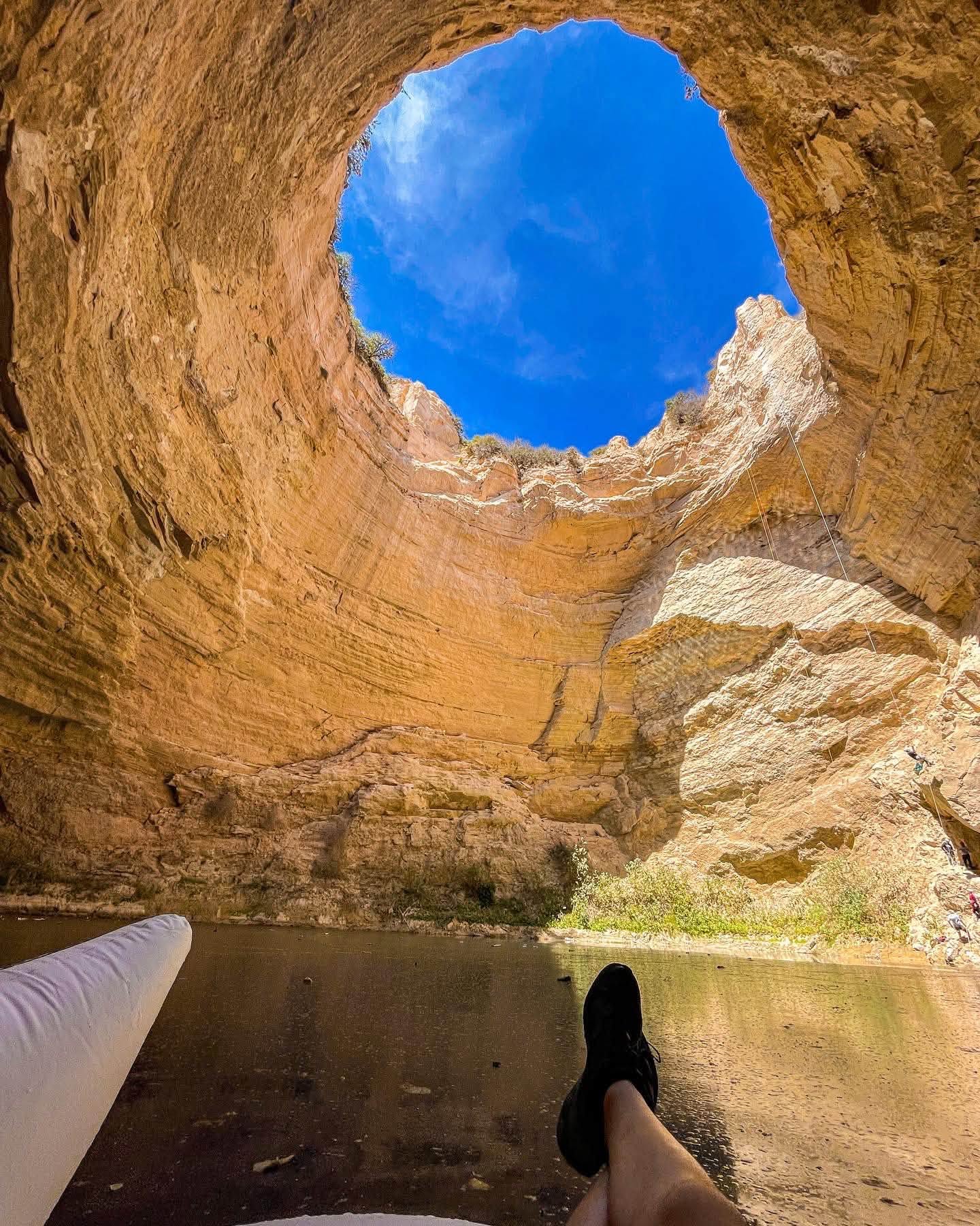 Vista Desde El Interior Del Pozo Del Gavilán En Galeana, Nuevo León, Mostrando Las Altas Paredes Rocosas, El Espejo De Agua Y La Abertura Circular Hacia El Cielo Azul.
