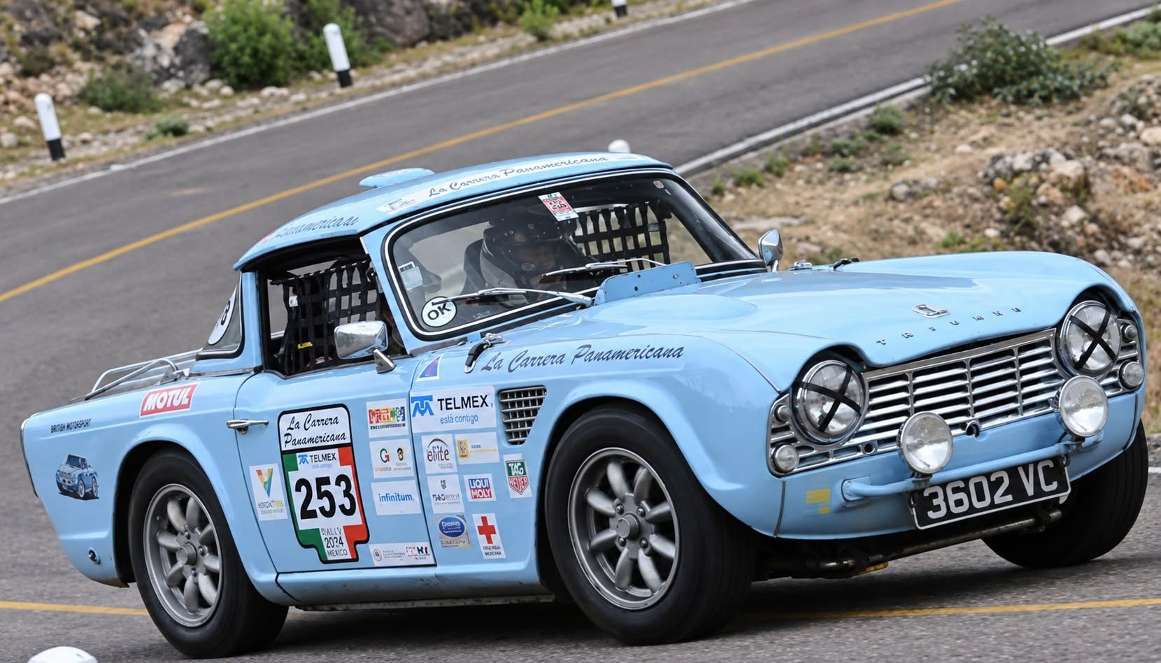 Automóvil Clásico De Competencia Color Azul Celeste Con El Número 253 Participando En La Carrera Panamericana Sobre Una Carretera Asfaltada.