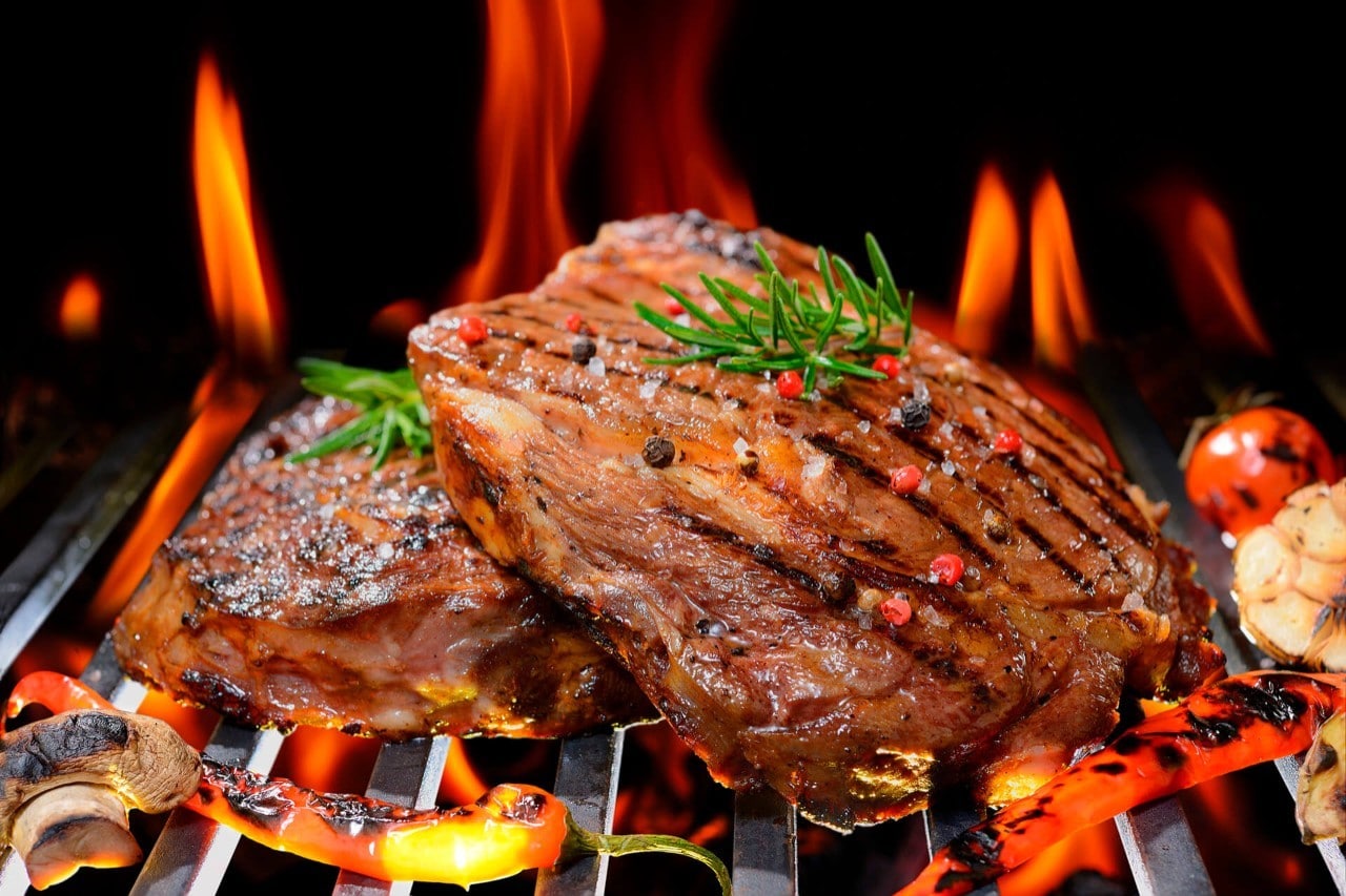 Cortes Gruesos De Carne De Res Asándose A La Parrilla Sobre Brasas Ardientes Con Llamas, Sazonados Con Romero, Pimienta Y Sal De Grano.