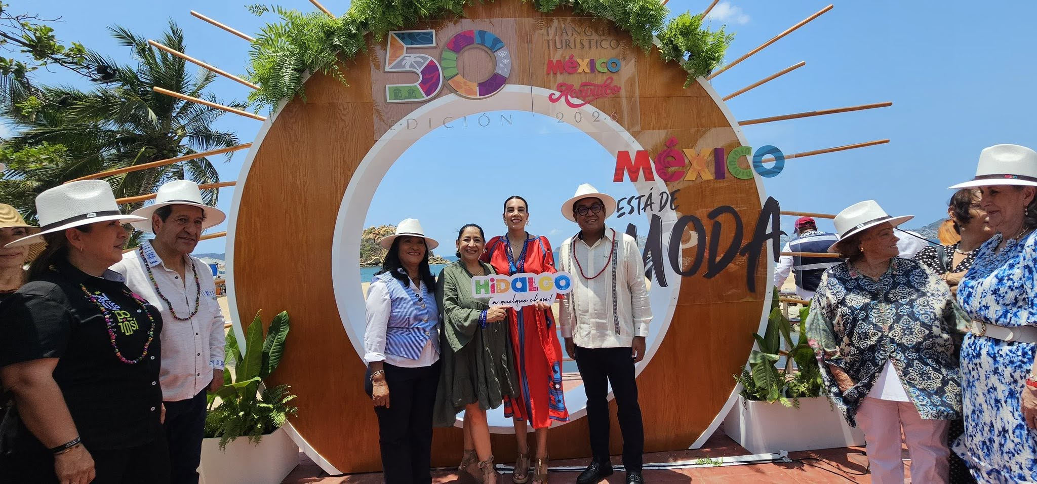 Un Grupo De Ocho Personas, La Mayoría Con Sombreros Blancos, Posa Sonriente Frente A Una Gran Estructura Circular De Madera Con El Texto &Quot;México Está De Moda&Quot; Y El Logo De &Quot;50 Edición&Quot; En Una Playa Durante El Tianguis Turístico 2025. En El Centro, Una Mujer De Rojo Sostiene Un Cartel De &Quot;Hidalgo&Quot;.