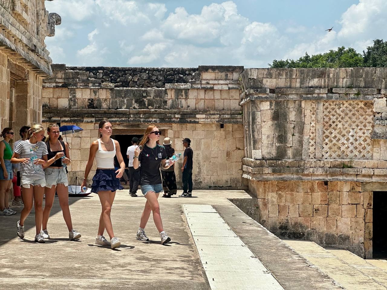 Turistas Caminando Por Una Explanada Con Estructuras De Piedra Antigua De La Cultura Maya En Yucatán.