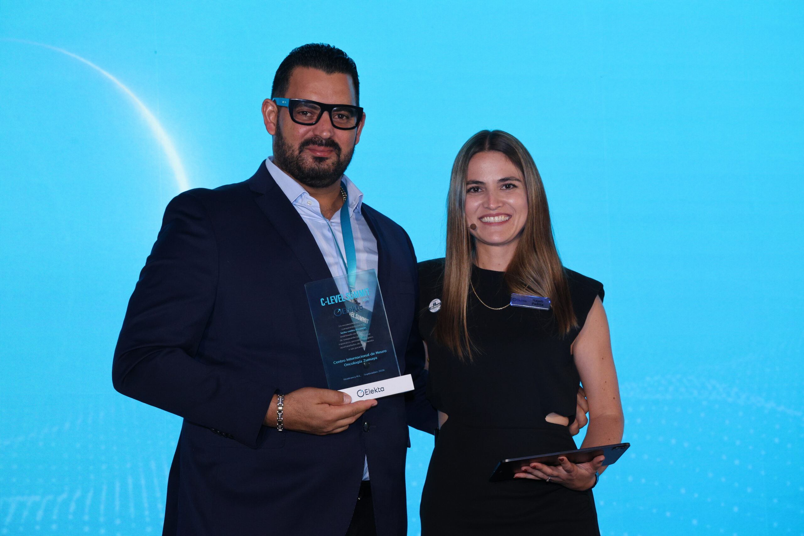 Representante De Hospitales Zumaya Sostiene El Premio Elekta 2026 Junto A La Presentadora En Monterrey.